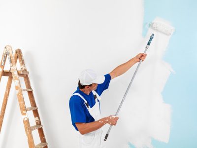 painter with cap painting a wall with paint roller and wooden vintage ladder, with copy space